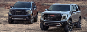The 2025 Yukon and the 2025 Yukon XL parked next to one another in a dirt lot